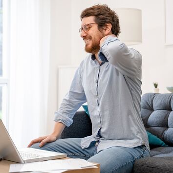 Ergonomie im Homeoffice Mann mit Nackenschmerzen durch unergonomischen Arbeitsplatz im Homeoffice
