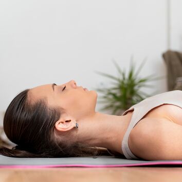 Progressive Muskelrelaxation nach Jacobsen Frau liegt entspannt auf dem Rücken und führt eine progressive Muskelrelaxation nach Jacobsen durch