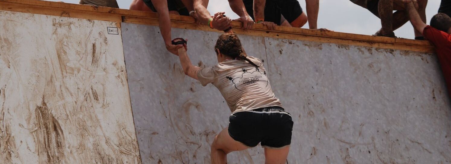 Ganzkörperfitness im Team mit Bootcampkurs Frau wird von 2 Männern die eine Mauer hinaufgezogen