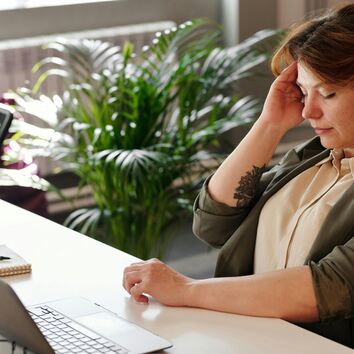 Vielsitzerseminar Frau greift sich an Schläfe, sie sitzt vor einem PC